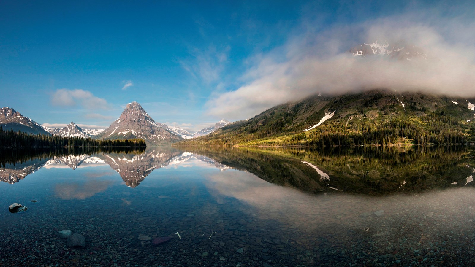 Snow-speckled mountains reflected into a calm lake.