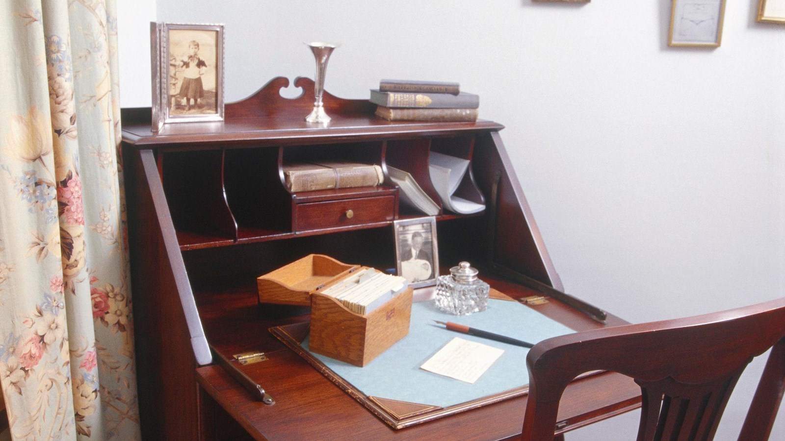 Drop-front desk and side chair with writing tools facing corner of room next to window