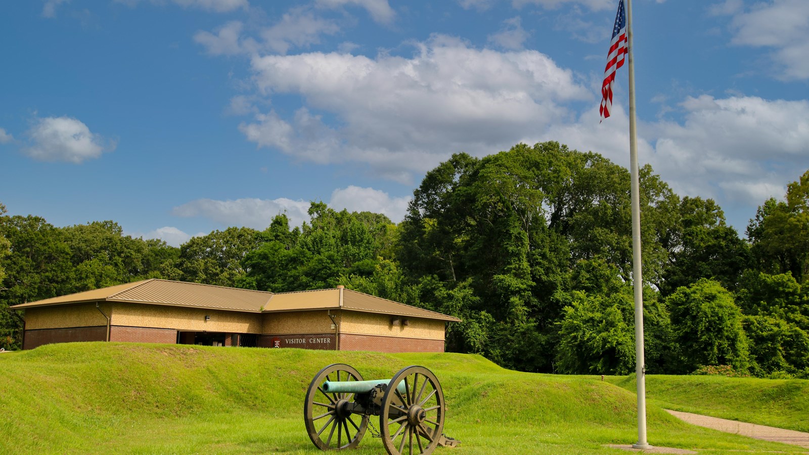 An image of a visitor center building with a cannon and flag pole out front