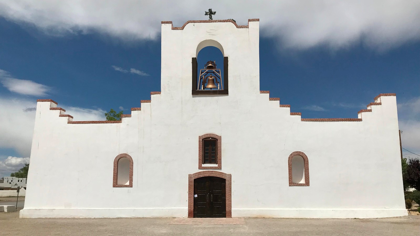 A white adobe one-story spanish mission with a single bell tower.