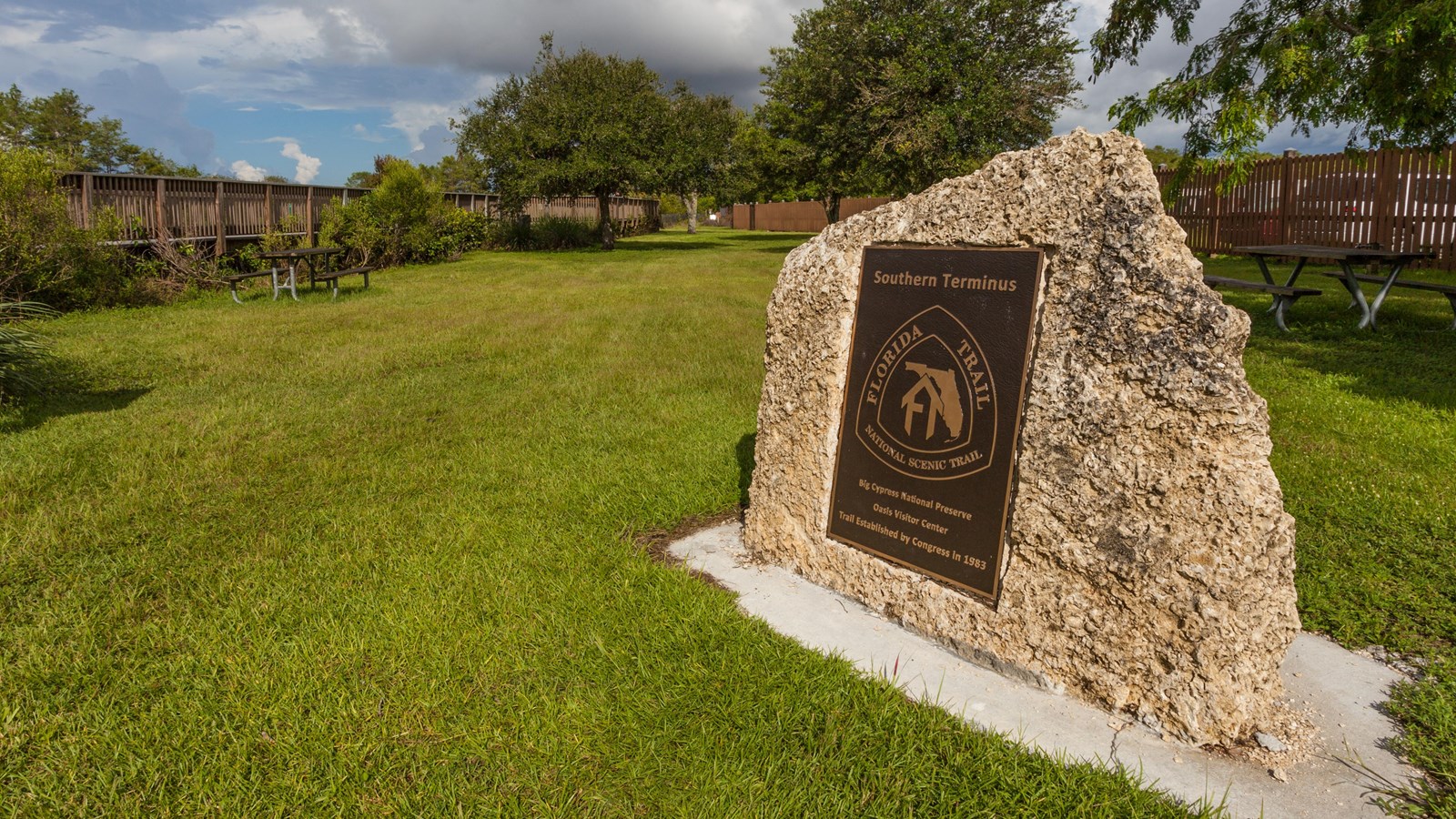 A large stone with a trail sign made of metal fixed on the surface next to a gravel path.