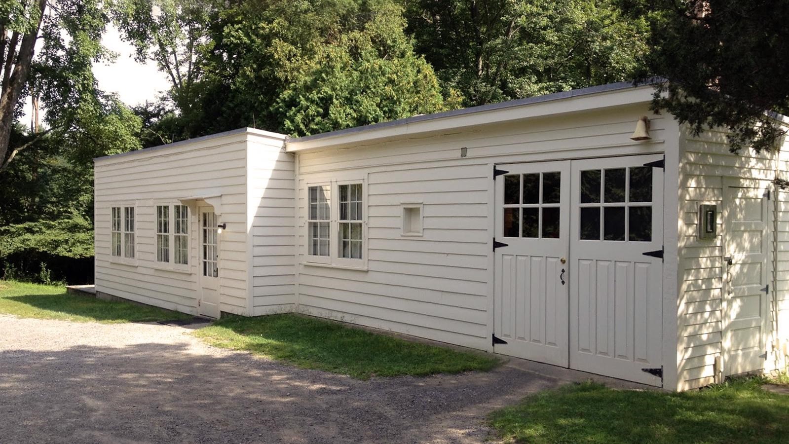 A single story white painted wood building with large windows and a double garage door.