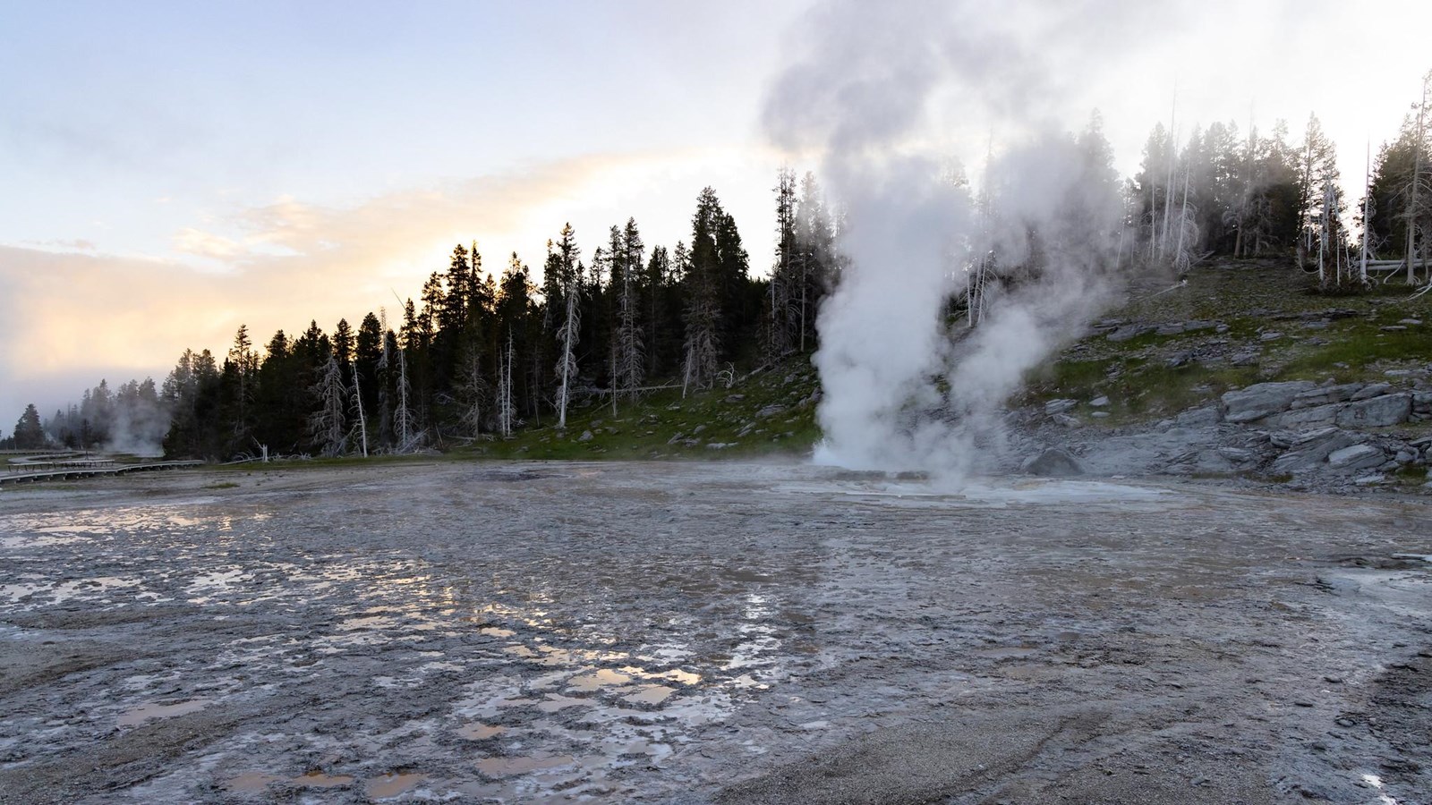 Steam rises off of a geyser in a thermal basin at sunset.