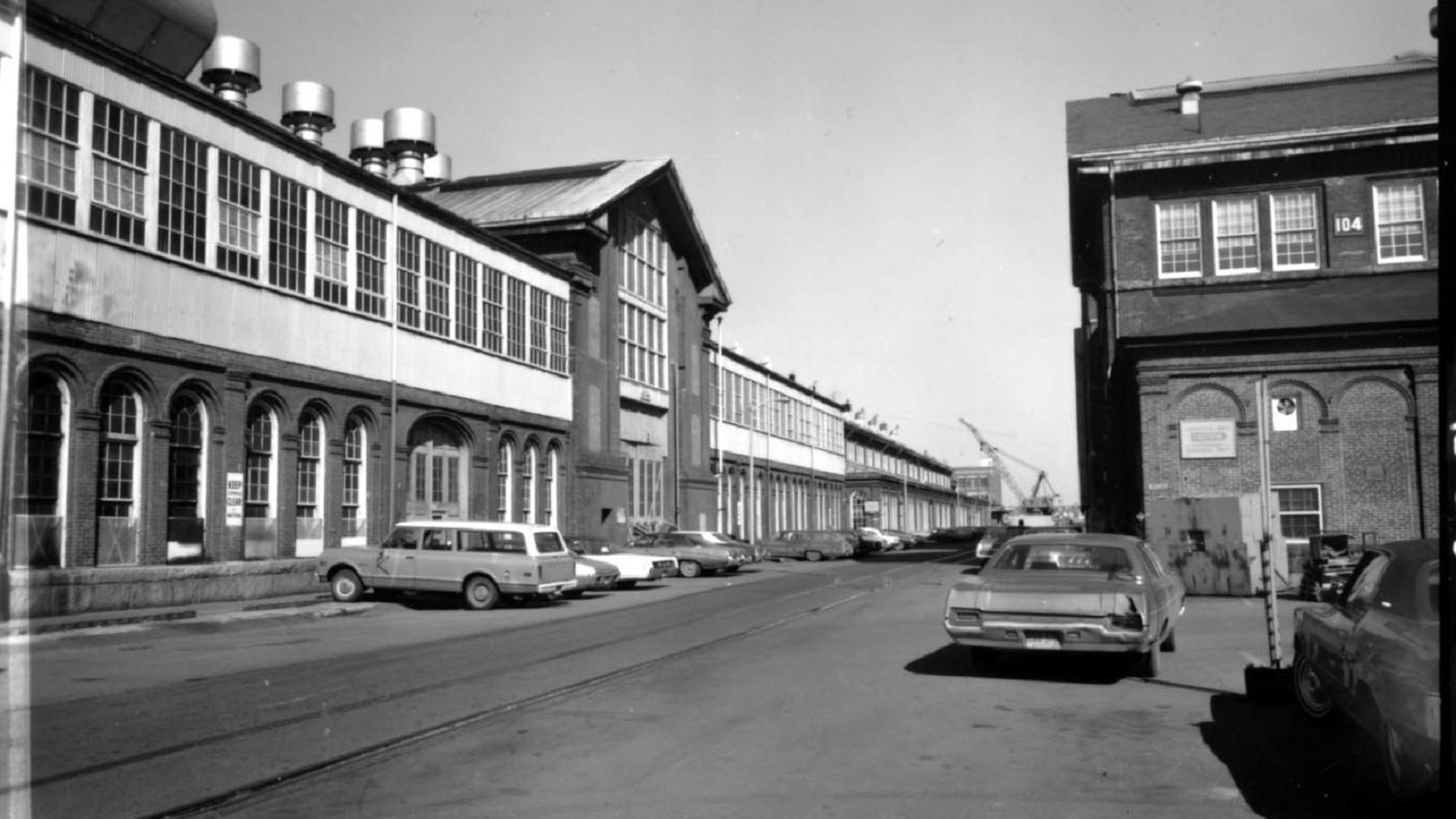 Black and white photo down a street with a tall two-story building that continues down the street.