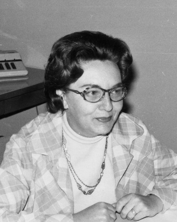 A black and white image of a woman with short hair and glasses wearing a plaid coat