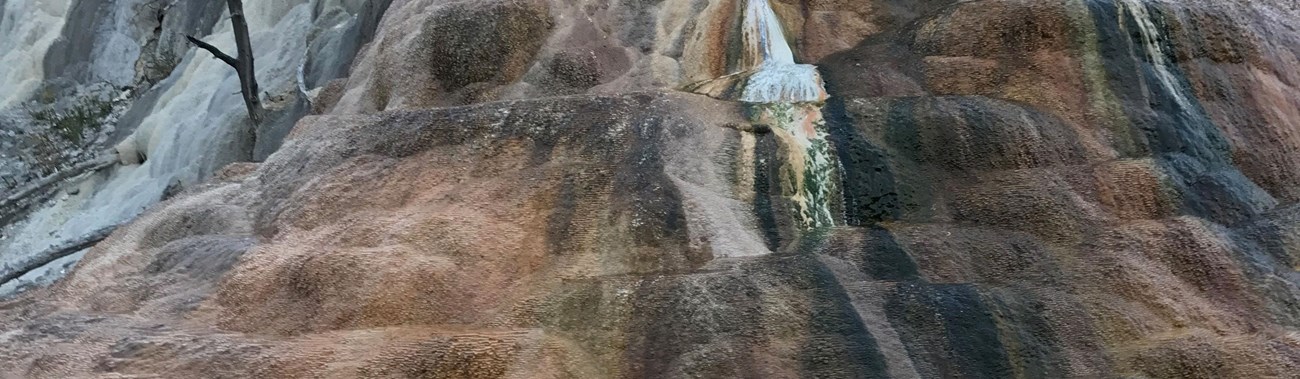 Streaks of white, orange, and green run down the sides of a large travertine mound.