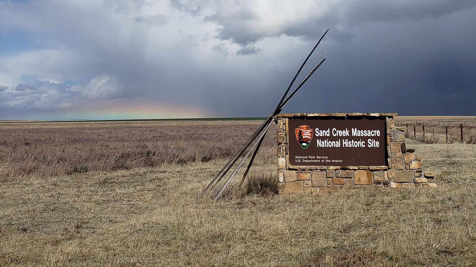 A rainbow is below a large thundercloud on the horizon. 