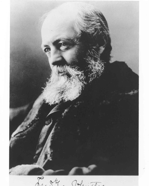 Elderly man with white hair on back of head but not on top, and white beard poses for photograph.