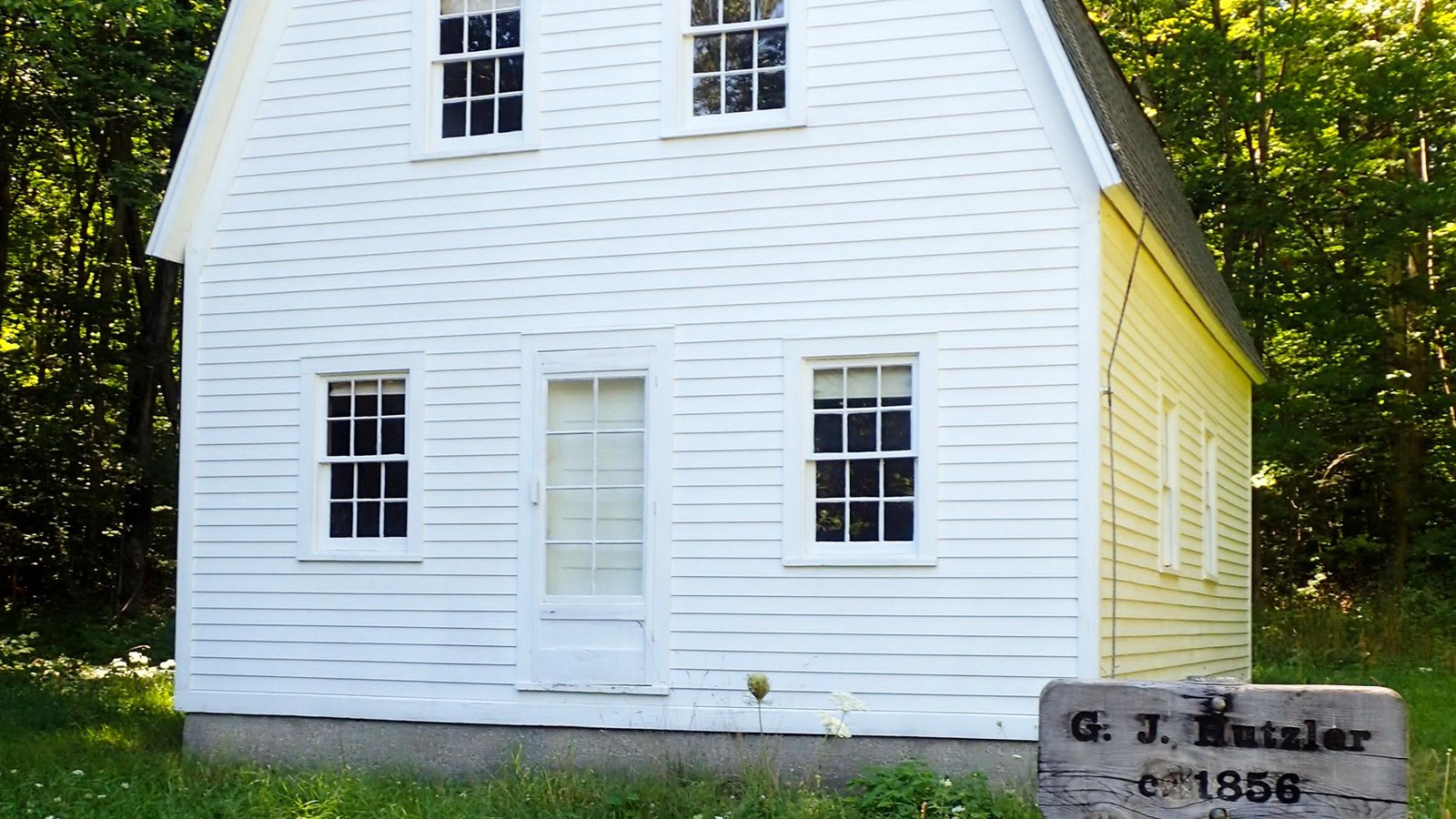 White barn-shaped farmhouse with old wooden sign say G. J. Hutzler c. 1856