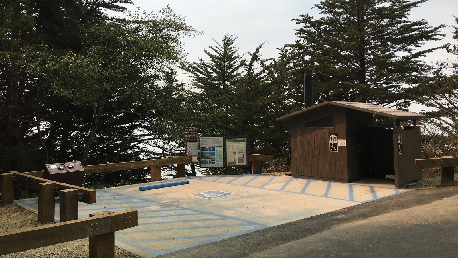 Brown building, parking area and wooden fence.