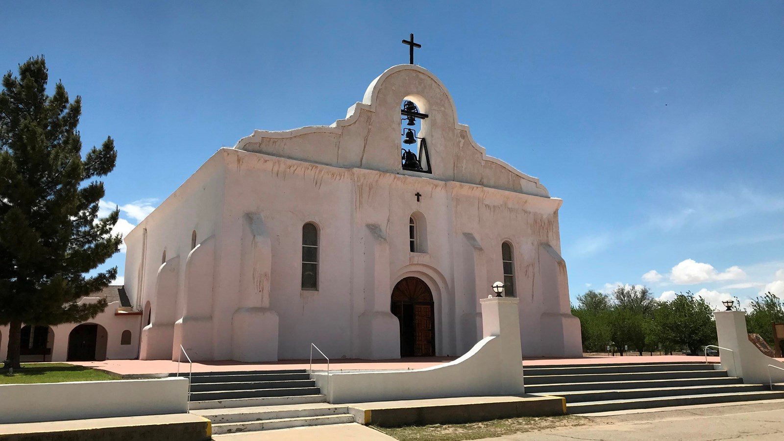 A large white adobe church with a large bell tower and cross at the top.