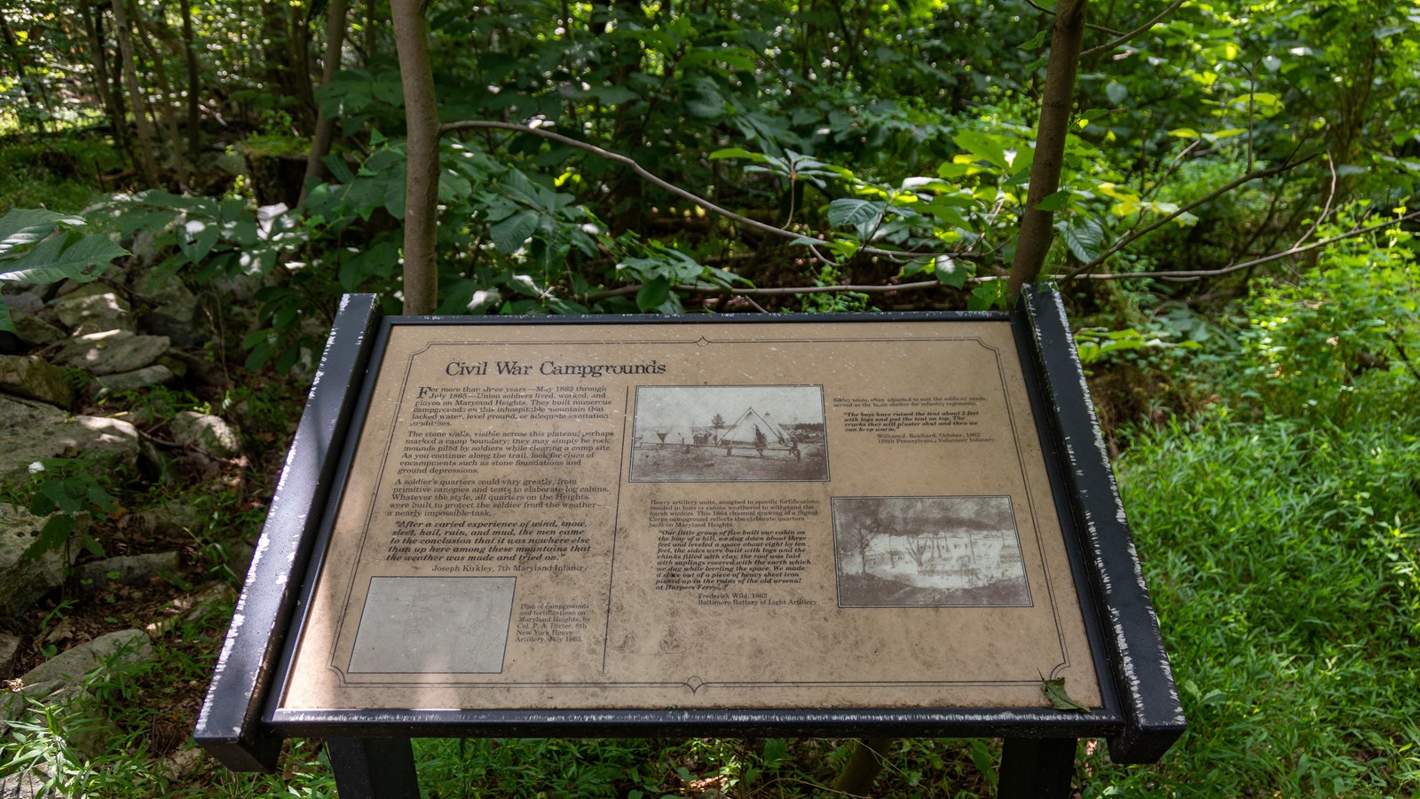 A sign next to a stone wall, trees, and vegetation describes Union soldiers\' encampments.