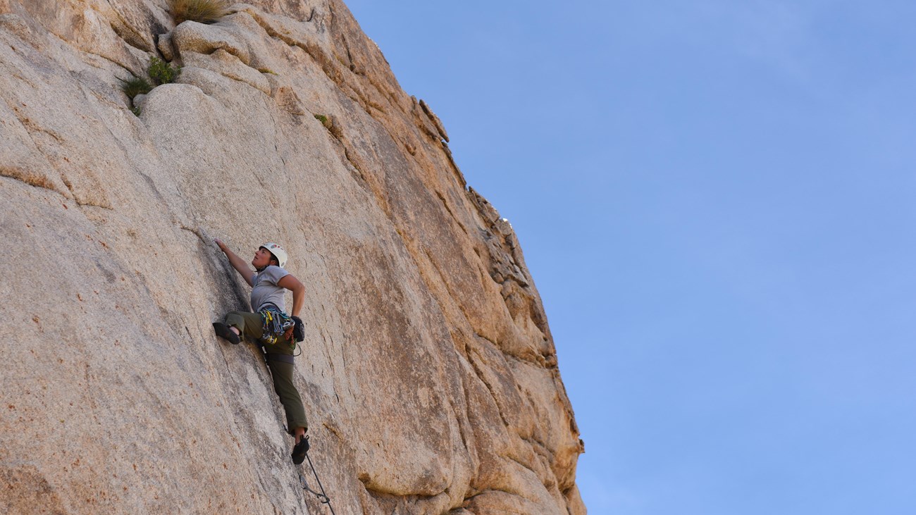 A rock climber making their way up a large tan rock face.