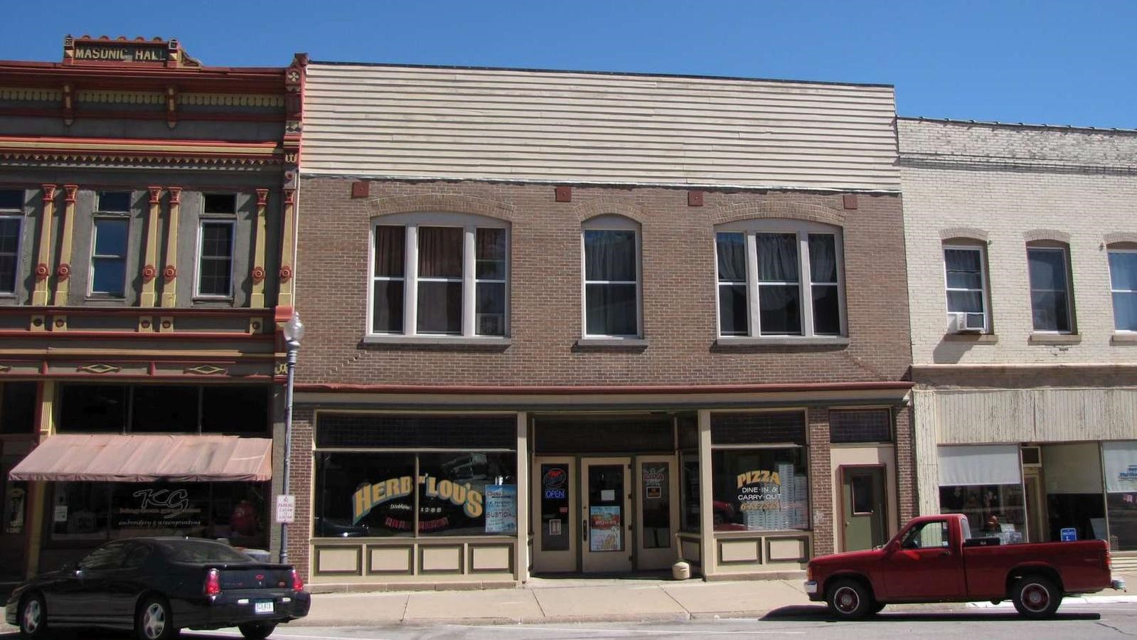 A former garage has two stories, with brick above a wooden storefront façade.