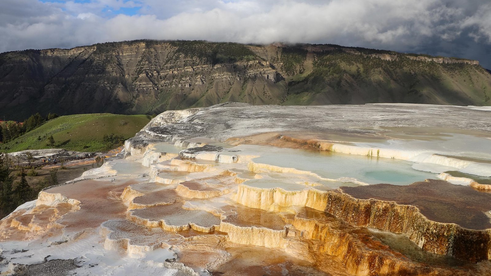 Colorful bacterial mats grow on travertine terrace formations with a mountain in the distance.