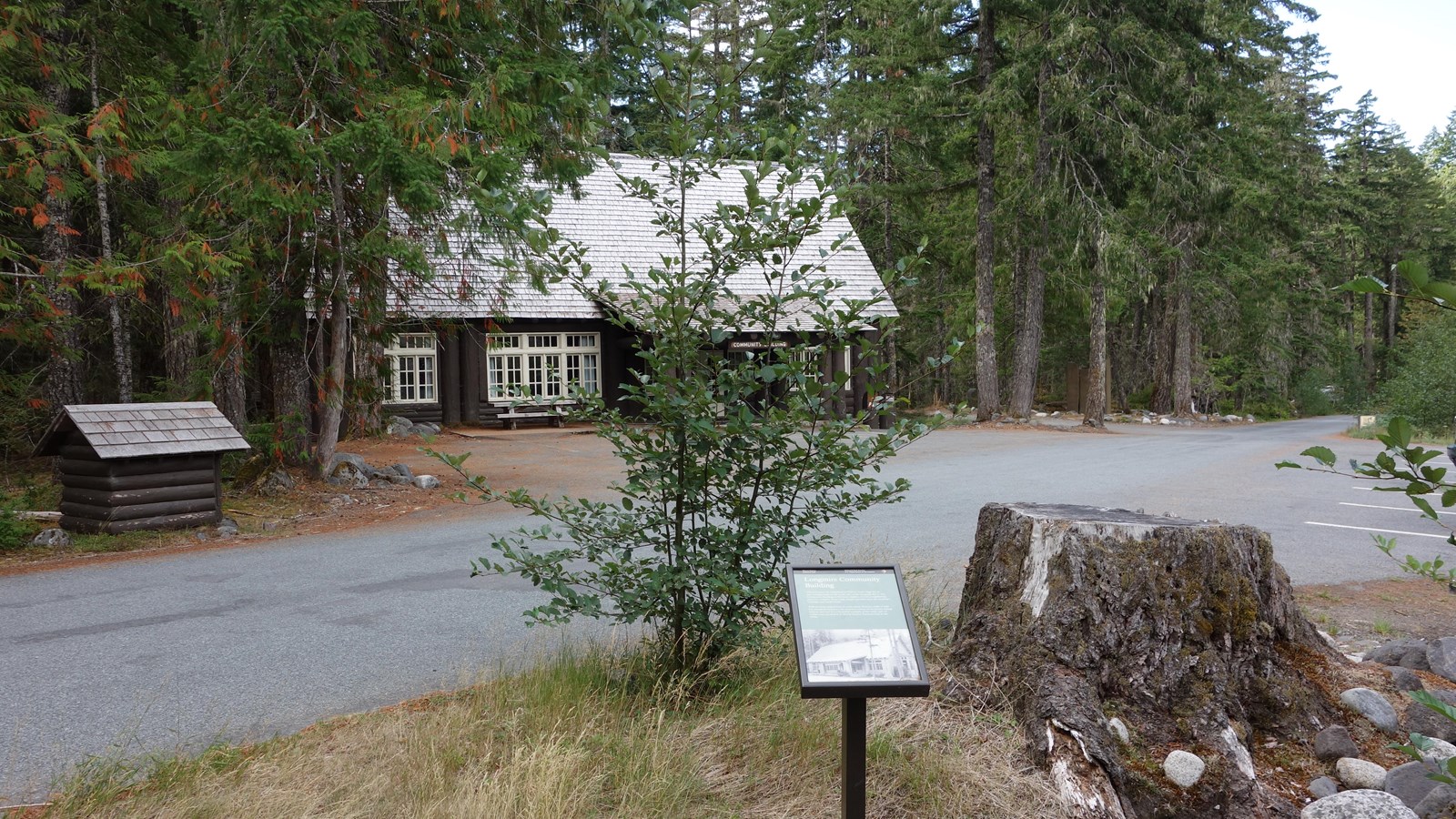 A wayside panel next to a road looking back over the road towards a large wood building.