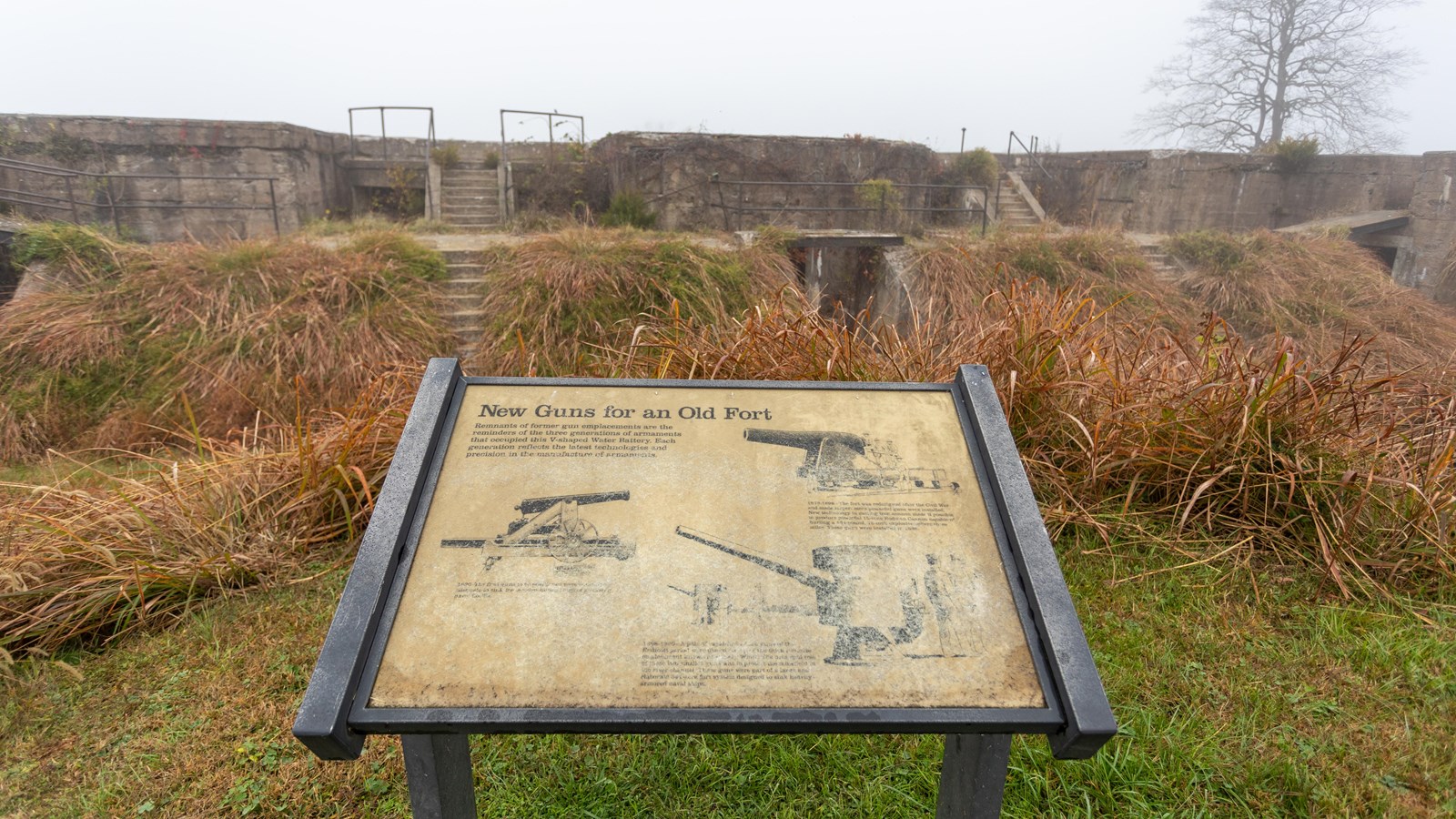 An interpretive panel stands in front of a concrete emplacement, with text and three illustrations.
