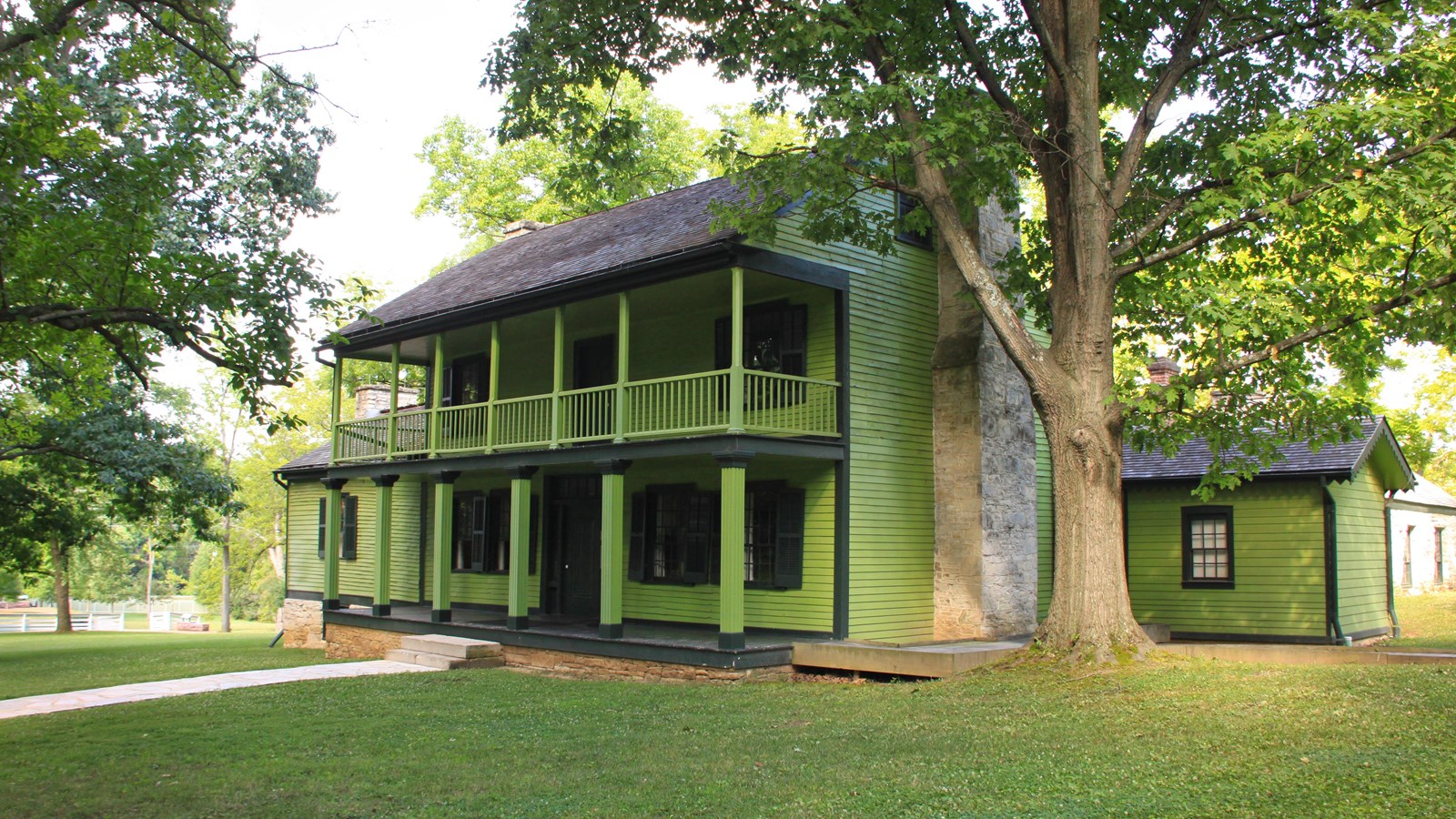Photo of a bright green, two-story house with a two story front porch, situated among several trees