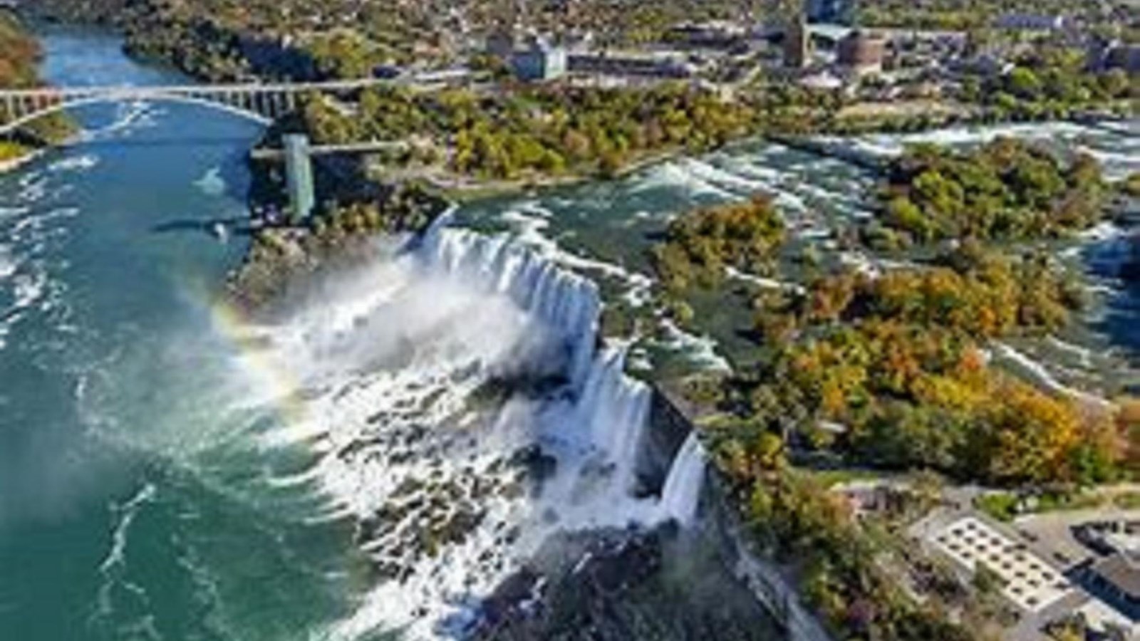 Aerial view of large waterfall with trees and city behind it.