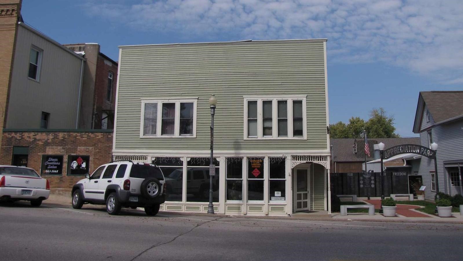 A light green downtown building has a light green wooden façade with white trim.