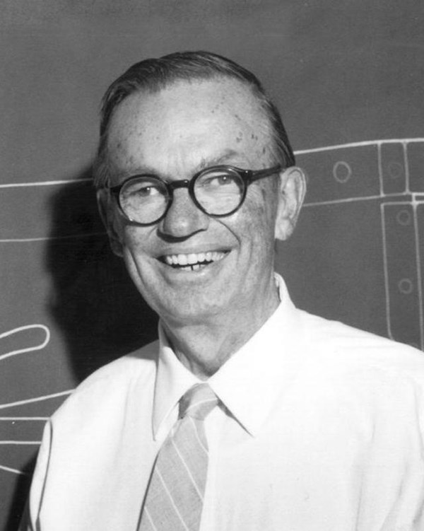 Man in white shirt, tie, and glasses, smiles
