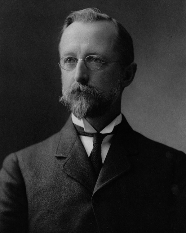 Man with short blonde hair in glasses and a suit poses for a picture