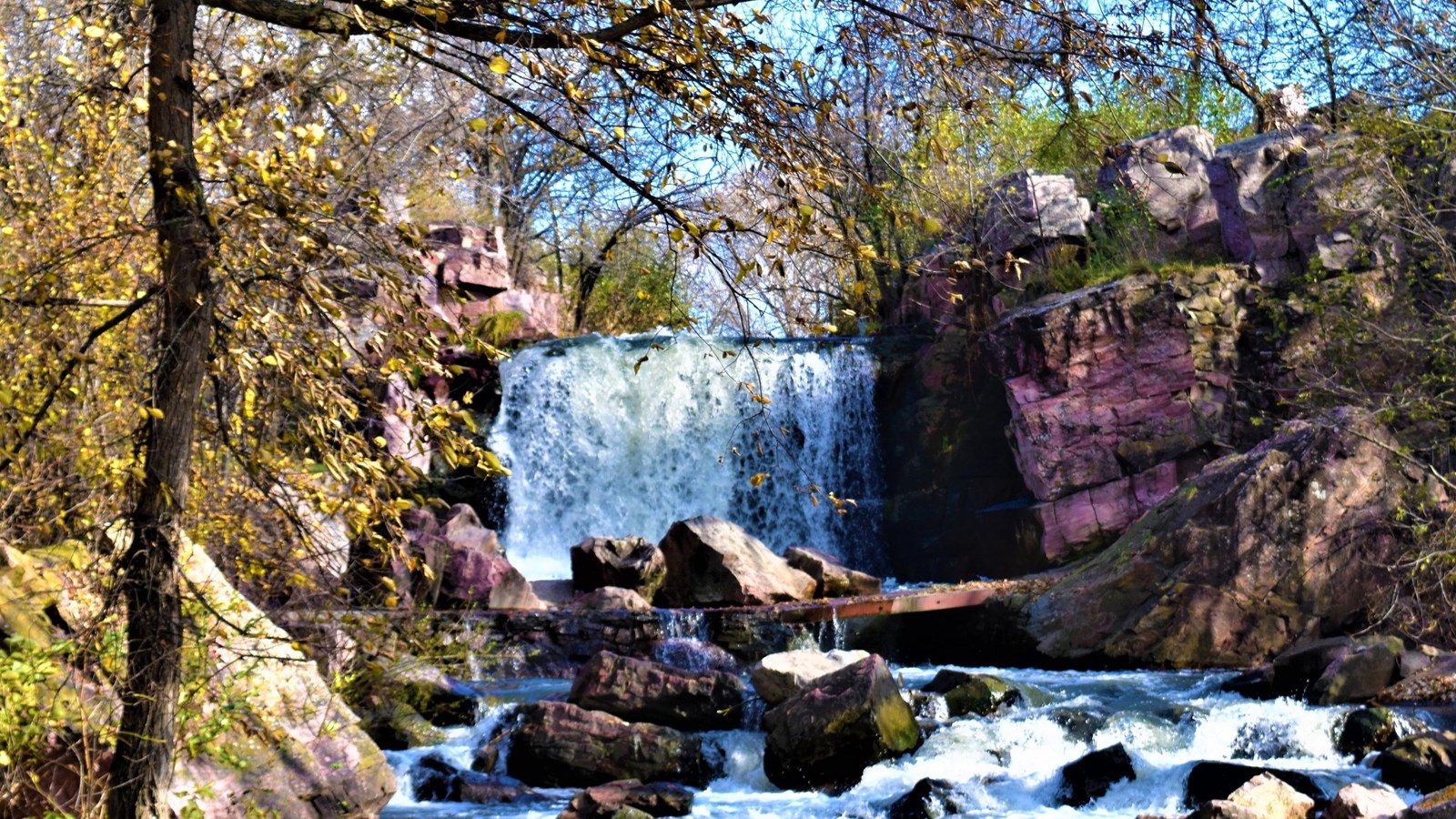 A waterfall surrounded by pink rocks and fall foliage.