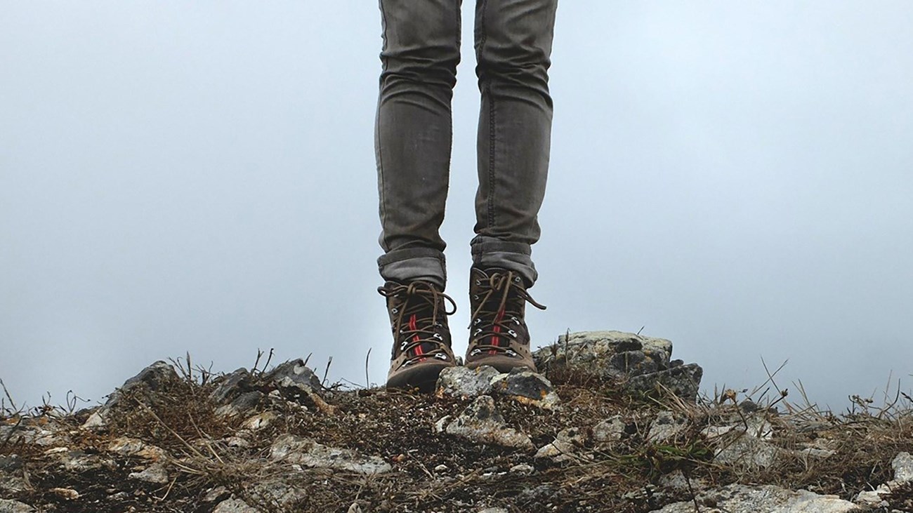A close up of a hiker\'s boots standing on a rock cliff.