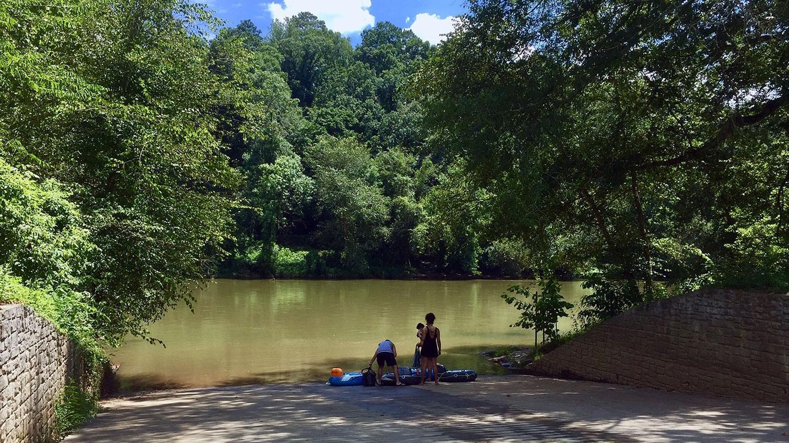Three people standing at the end of the boat ramp with wooded shoreline in the distance.
