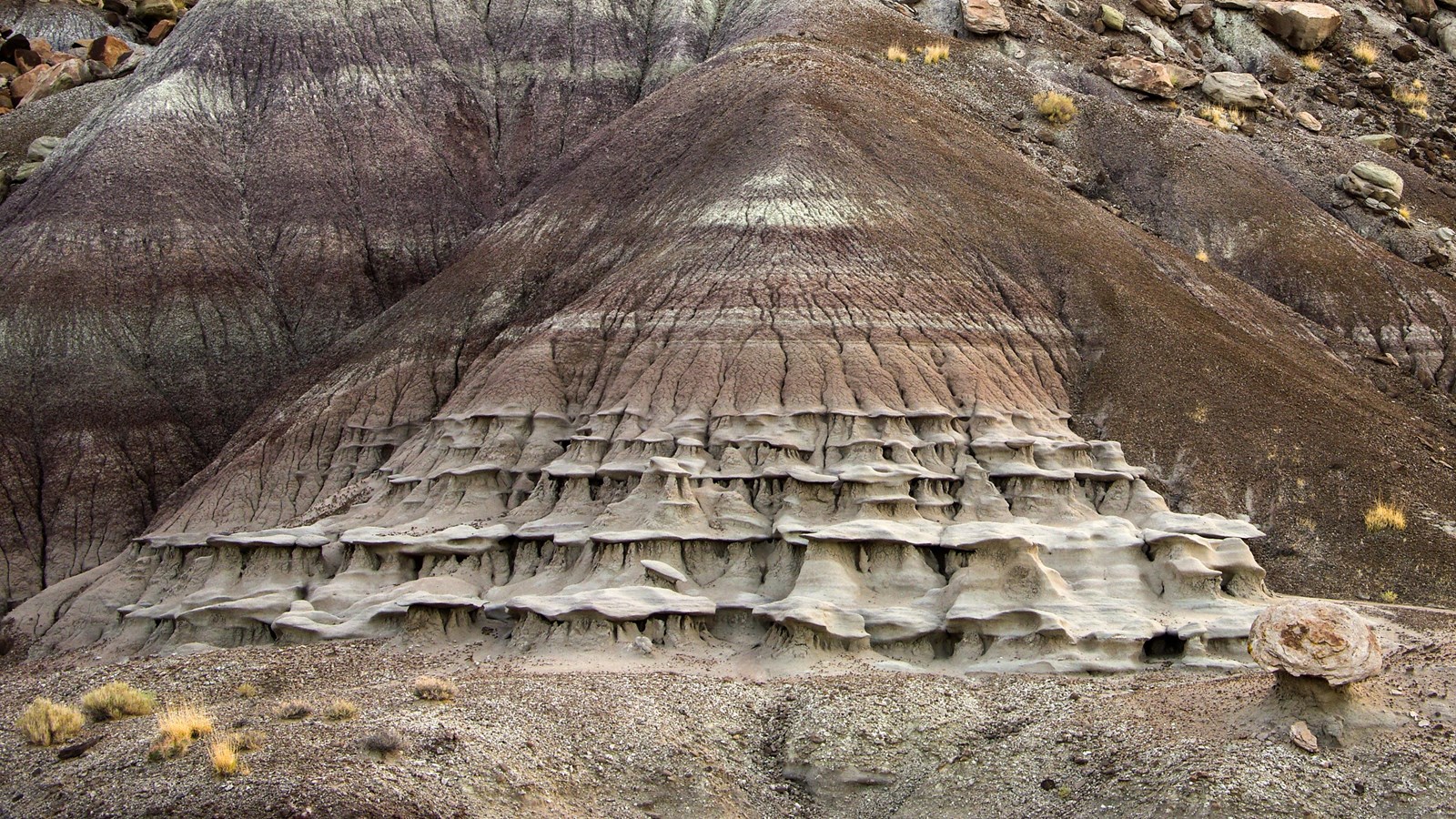 Ruffled sedimentary rock on a pyramidal hill against the side of a rocky mesa.