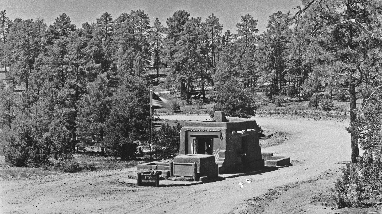 a stone building stands in the middle of a dirt road, a flag flies from a pole next to the building