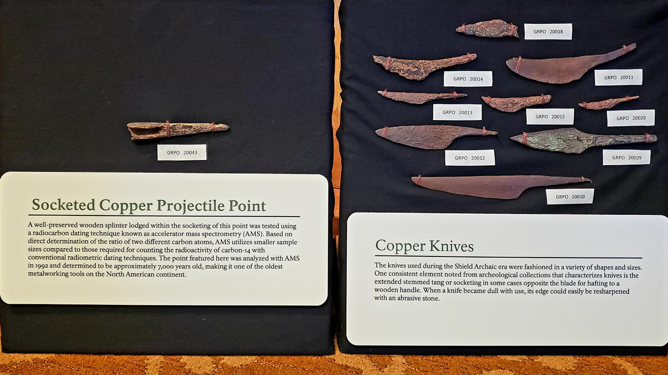 Weathered copper projectile point and knives in a display case.