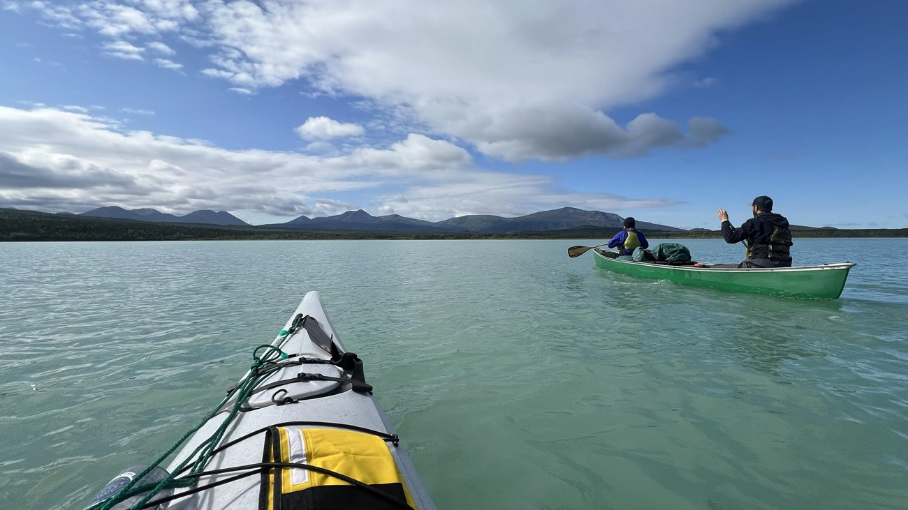 two boats glide through aqua waters toward a mountain range.