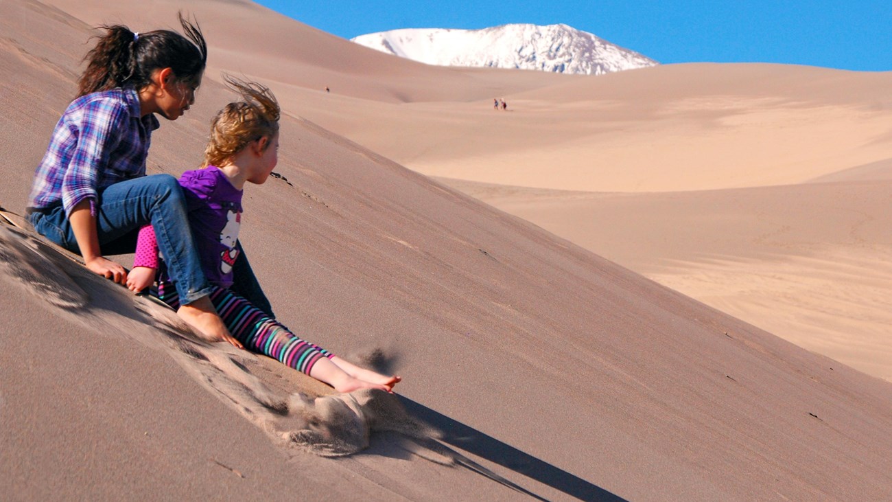 Two girls speed down a dune on a specially designed sand sled. 