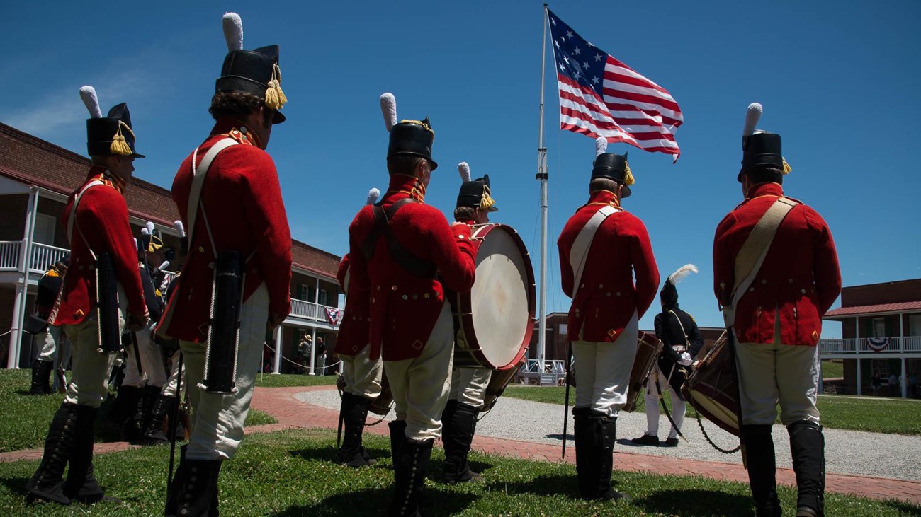 A group of living historians stand in the fort with the large garrison flag flying in the background