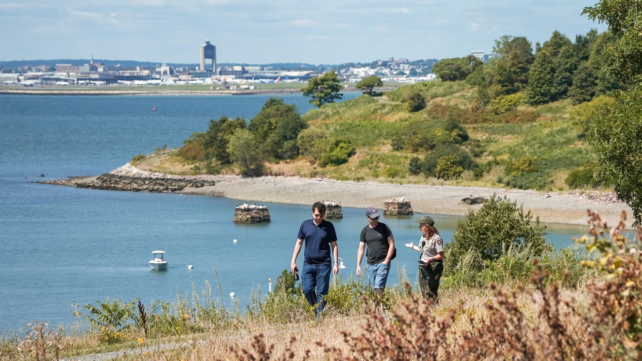 A ranger walks along a gravel path on an island talking to two other people