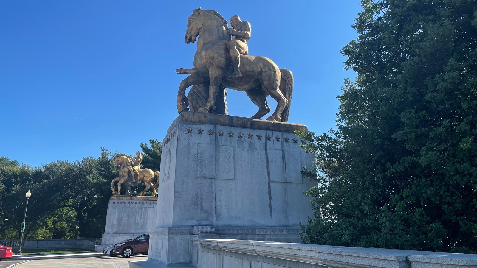 Large, gold statue of a two figures next to a winged horse, set on a large pedestal