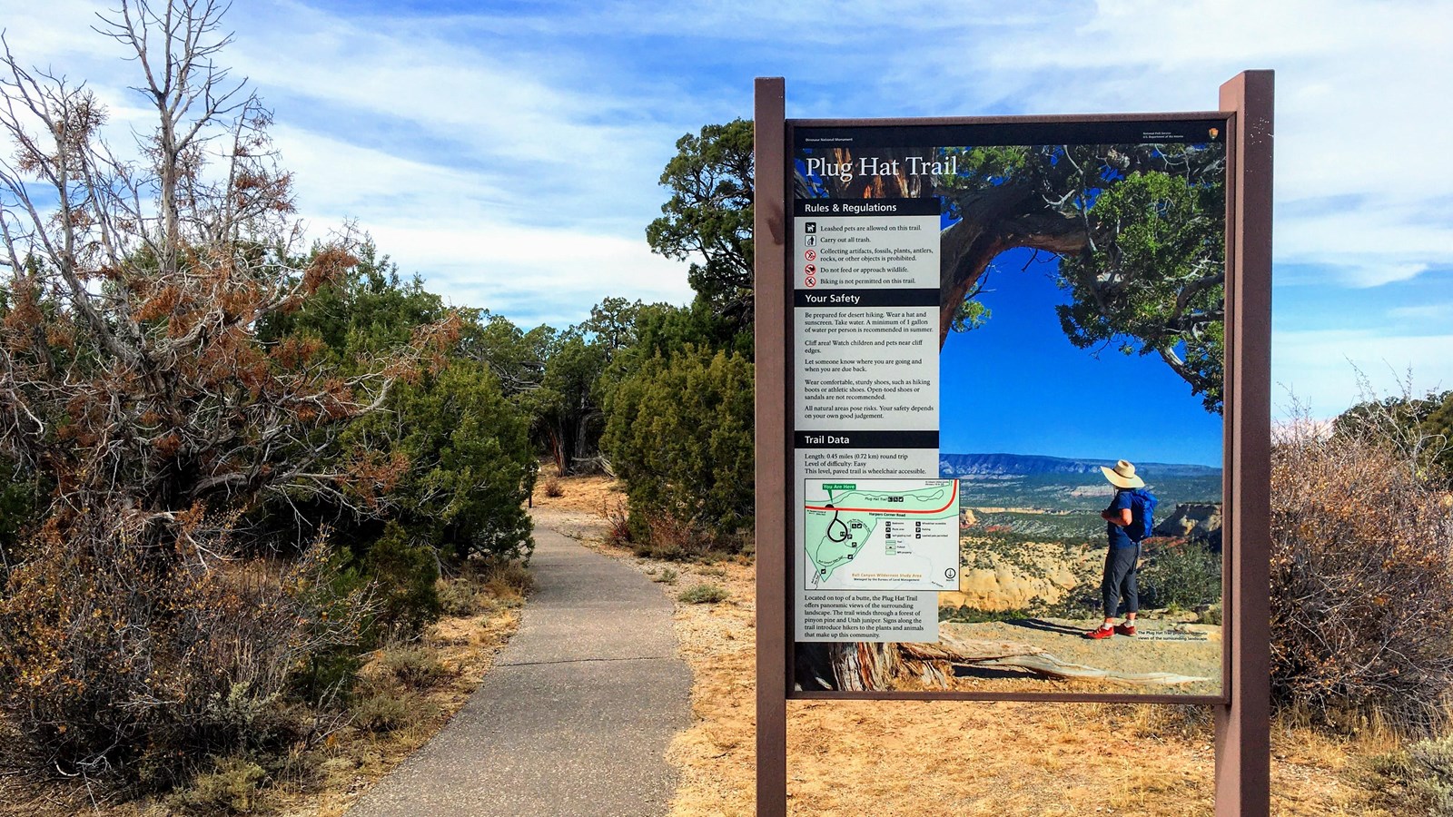 Informational sign and paved path at the Plug Hat Trailhead.