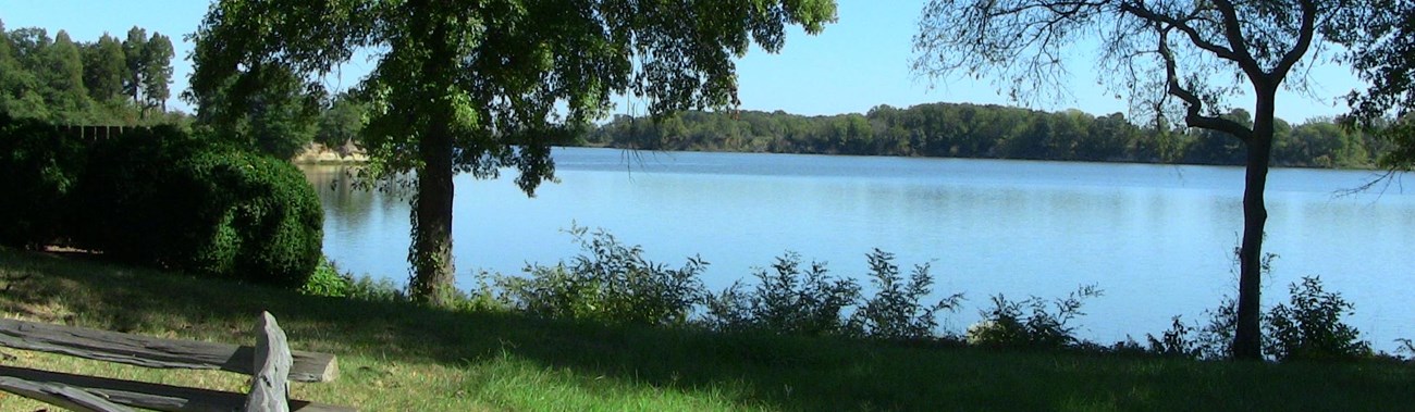 view of wide, tidal creek with trees and split rail fence in foreground