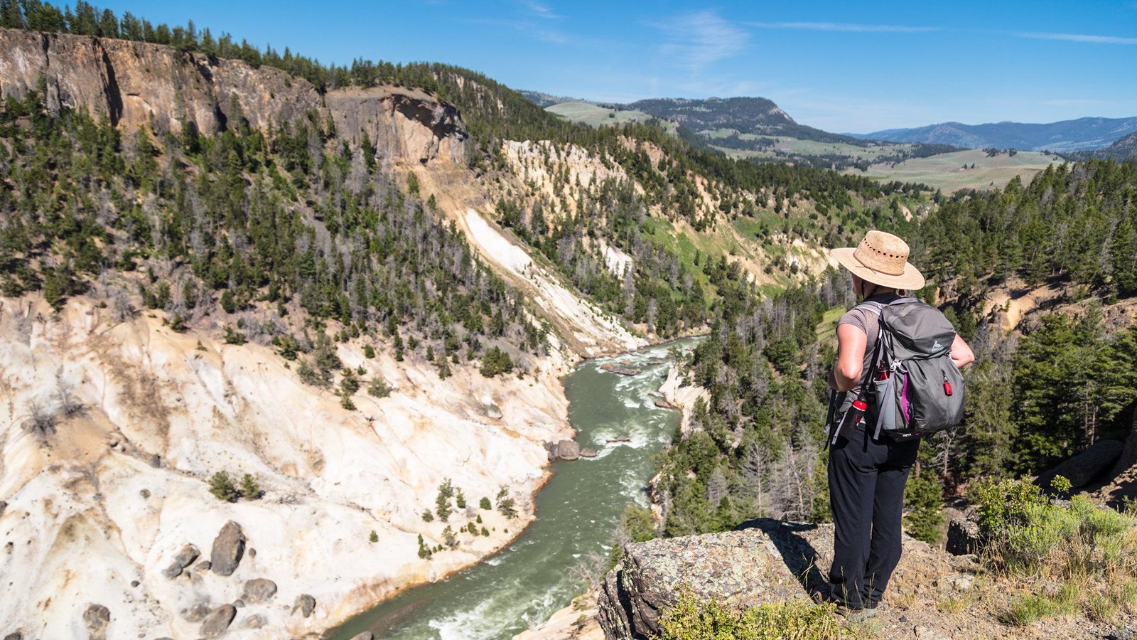 A hiker stands on the edge of a canyon and looks down at the river below.