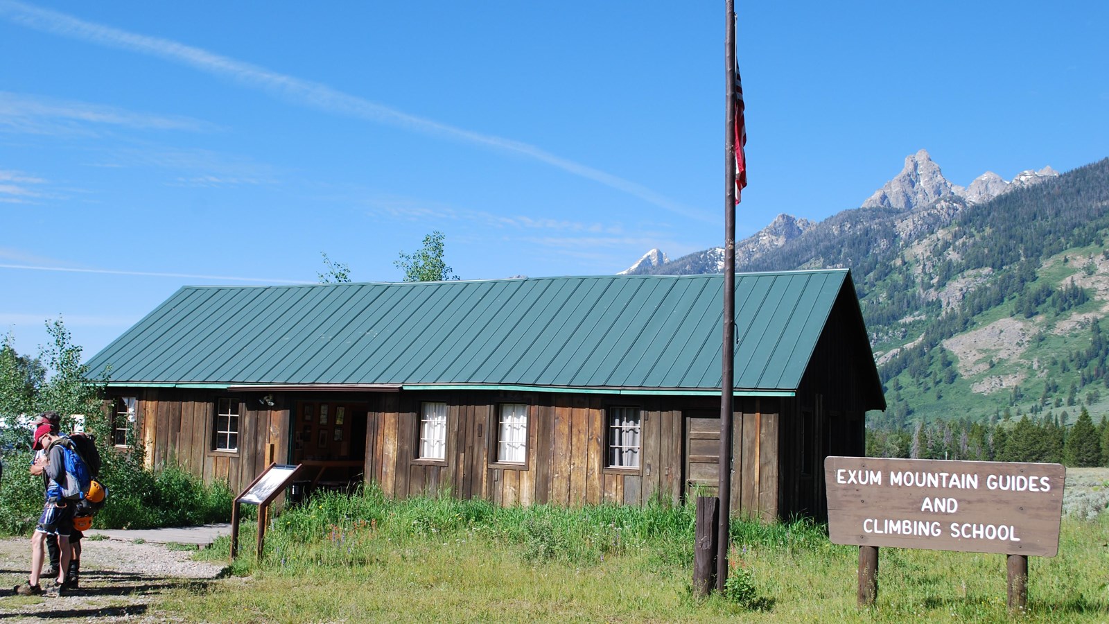 Exum Mountain Guides and Climbing School with a flag pole, a sign with the name, and mountains.