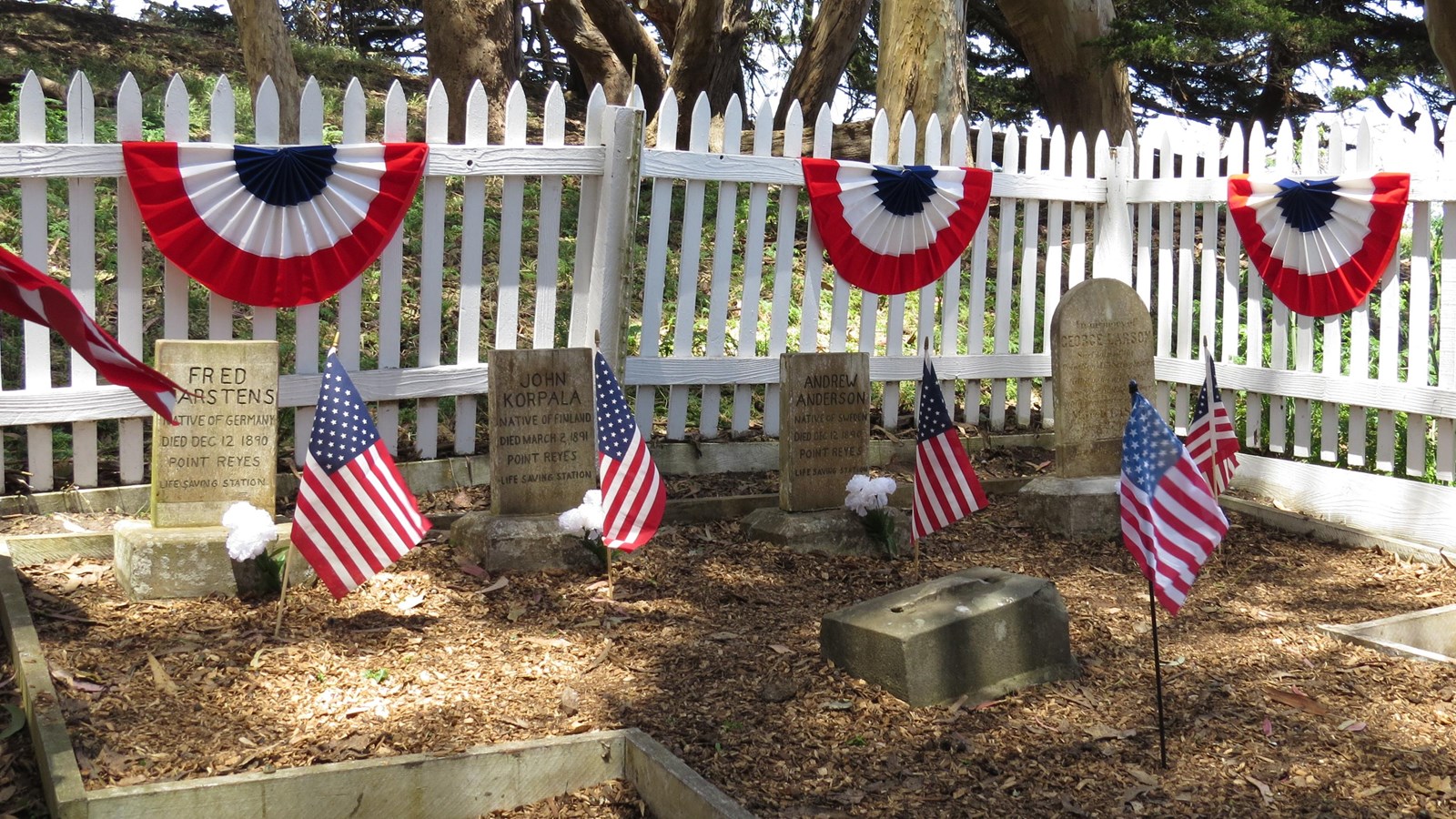 A white picket fence with red-white-and-blue bunting surrounds a tiny cemetery.