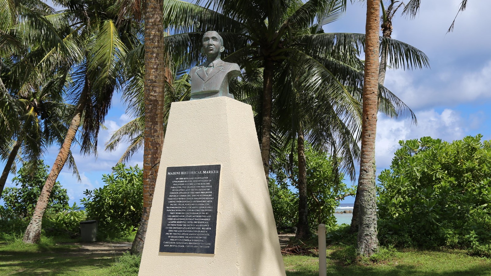 A beige obelisk with a metal plaque attached to the front and the bust of a man on the top.