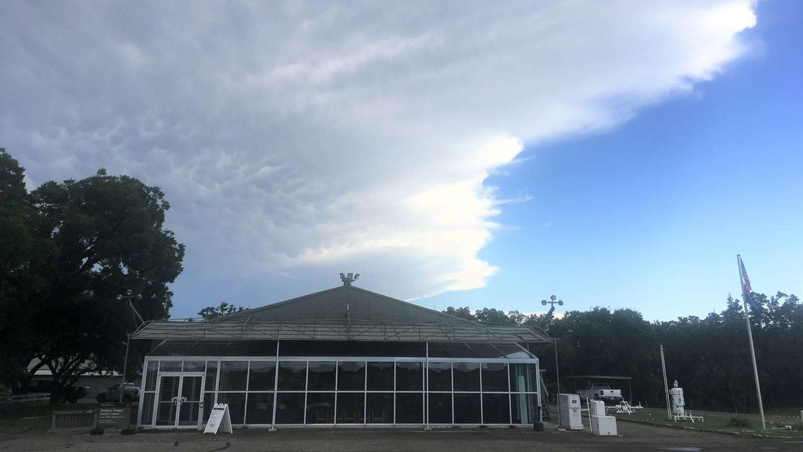 A large cloud sits above the gable roof of a large green building with glass windows.
