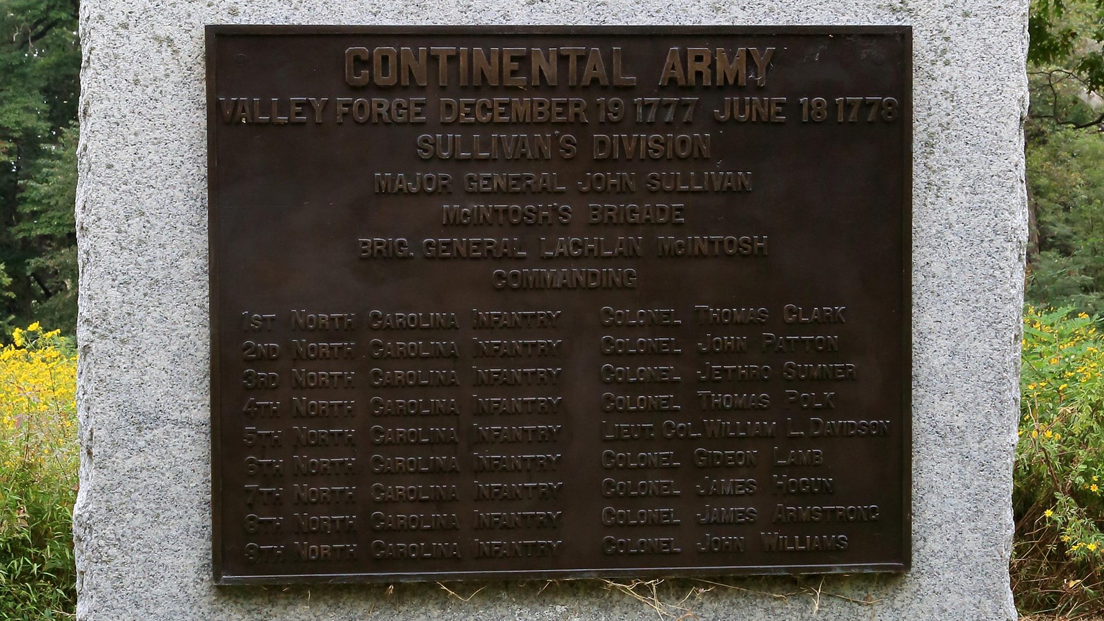 A large, smoothed granite block with a bronze plaque, sides and bottom rough.