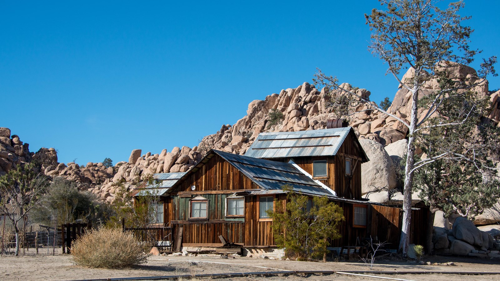 An old wooden two story ranch house with a metal roof in front of a large rock formation.
