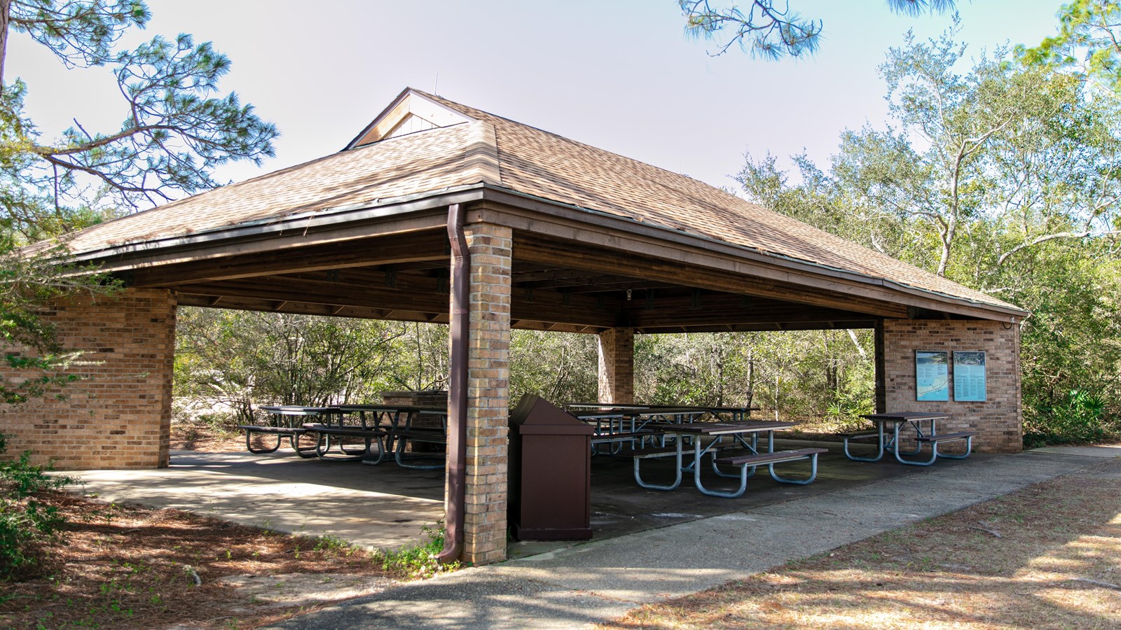A brick pavilion stands on a concrete pad amongst a forest.