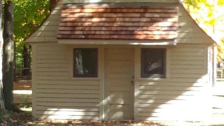 a small beige barn building that has two windows and a door on the front