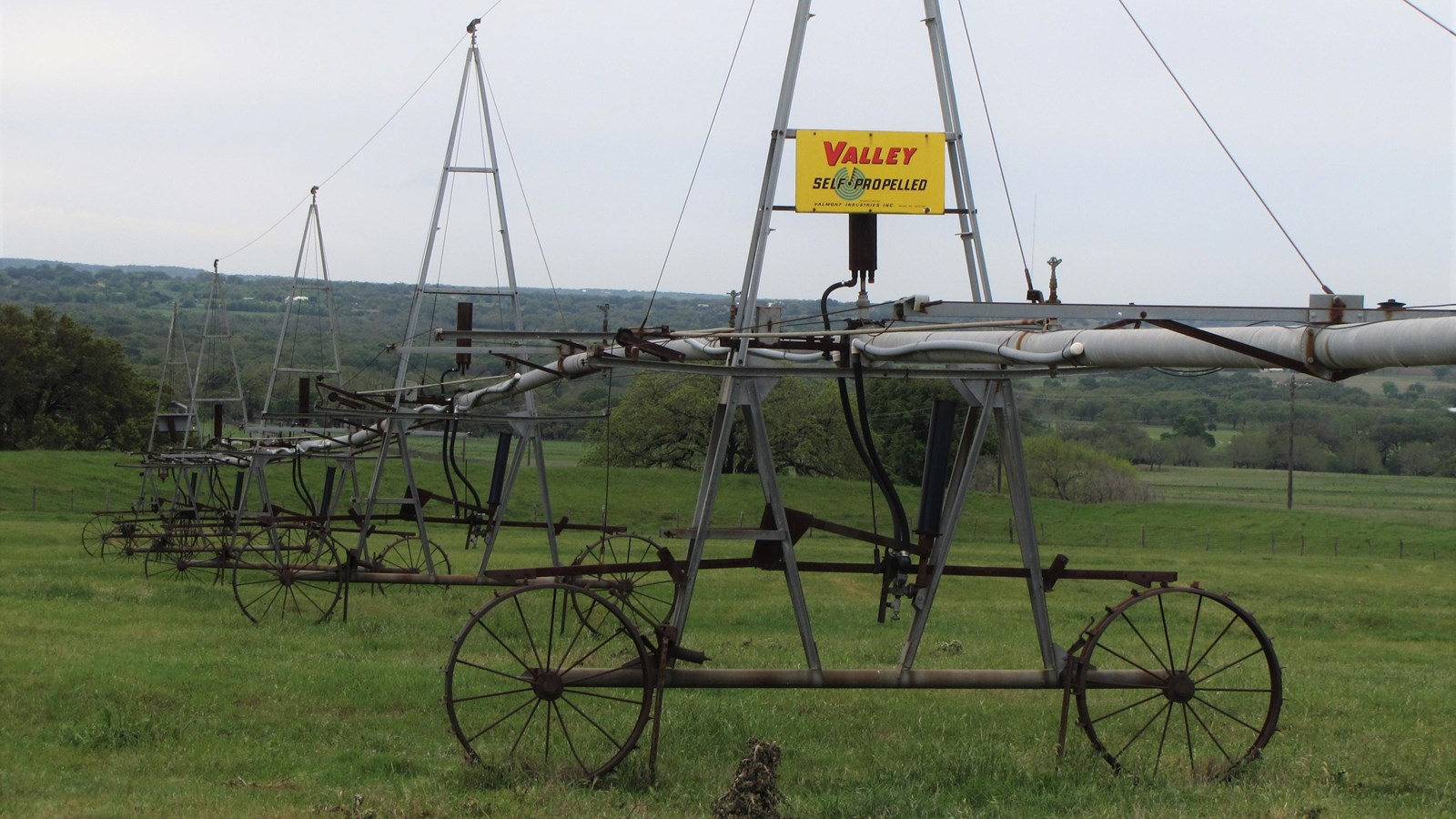 A metal irrigation apparatus stands on wheels in a green field.