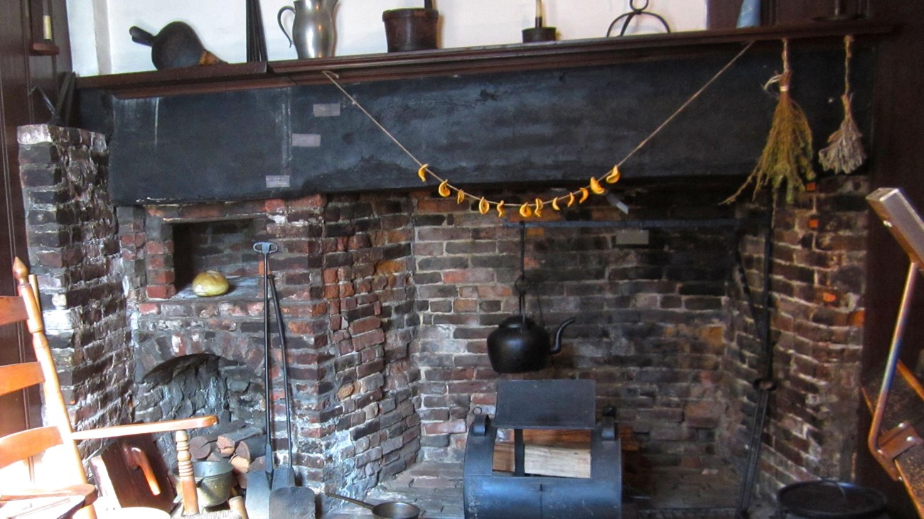 A wooden chair next to a brick fireplace with a wood mantle that has cups on top